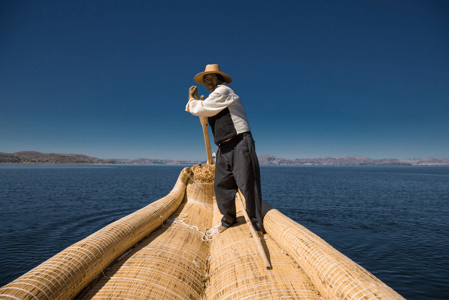 Indigenous man wearing a straw hat steering a large reed boat on Lake Titicaca