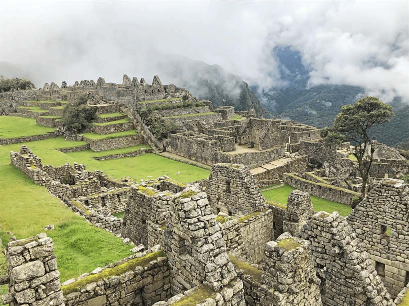 Ancient Incan buildings without roofs within Machu Picchu complex with low clouds covering mountains in the background