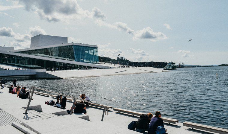 People relaxing by the water on a sunny day near the National Opera House in Oslo