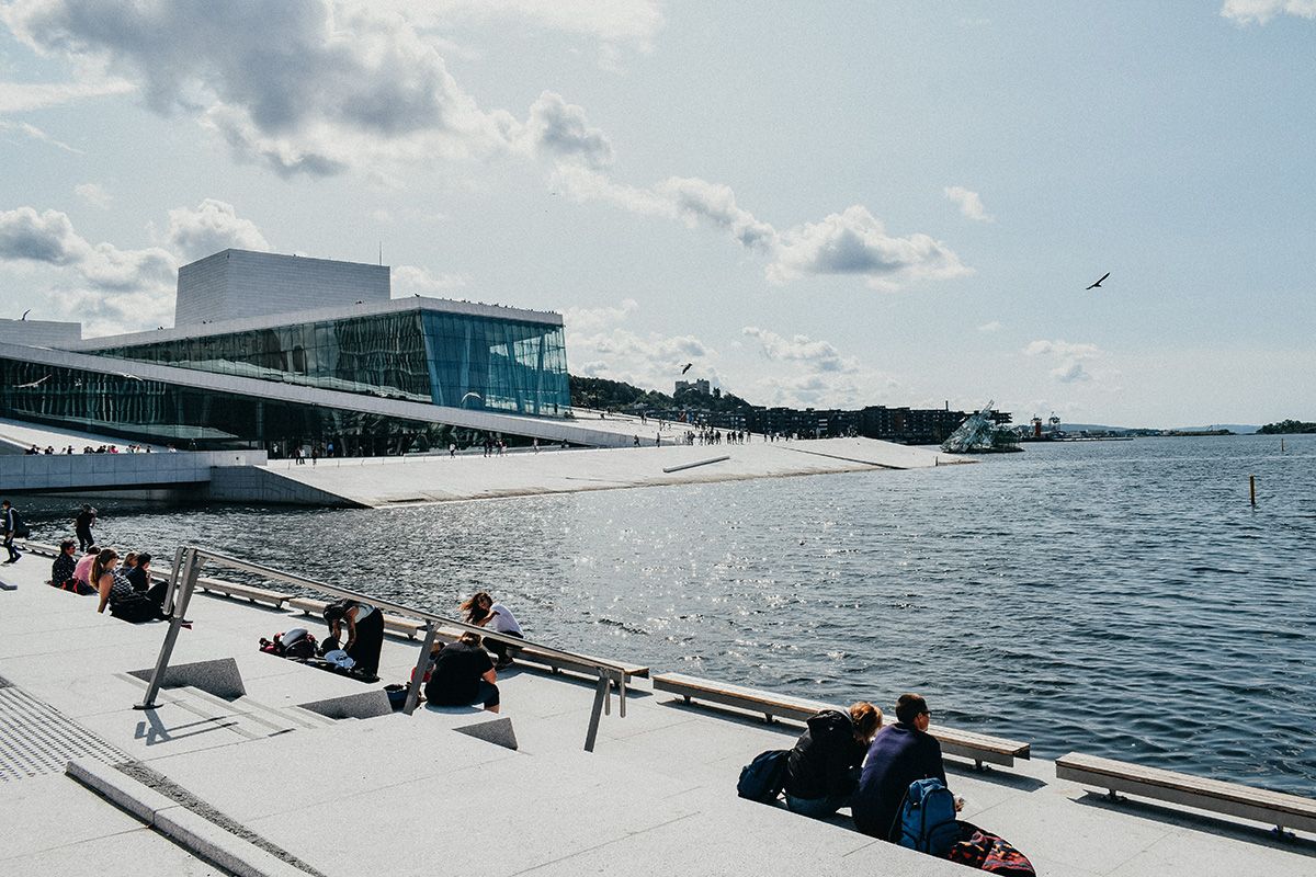 People relaxing by the water on a sunny day near the National Opera House in Oslo