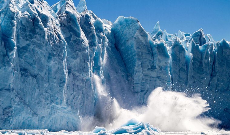 View from water level of a piece of the blue Perito Moreno Glacier falling into Lago Argentino causing a huge splash
