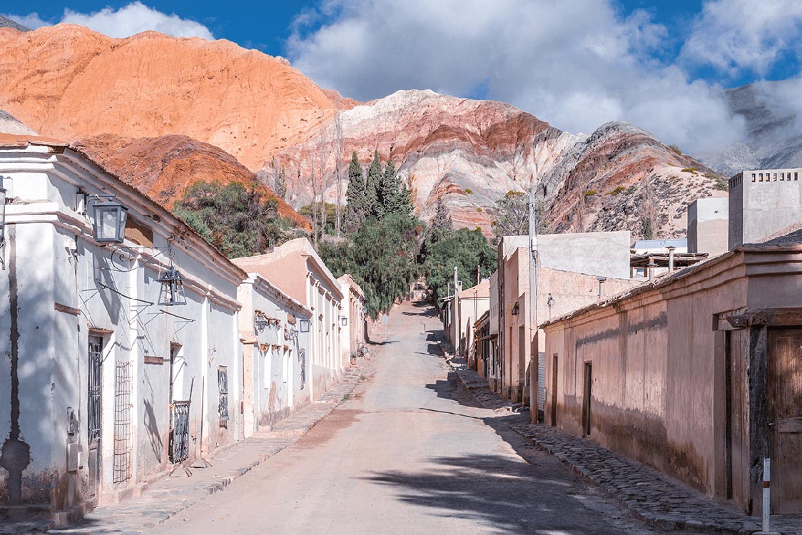 Street leading to the striped Hill of Seven Colored lined with white and brown buildings in the mountain town of Purmamarca