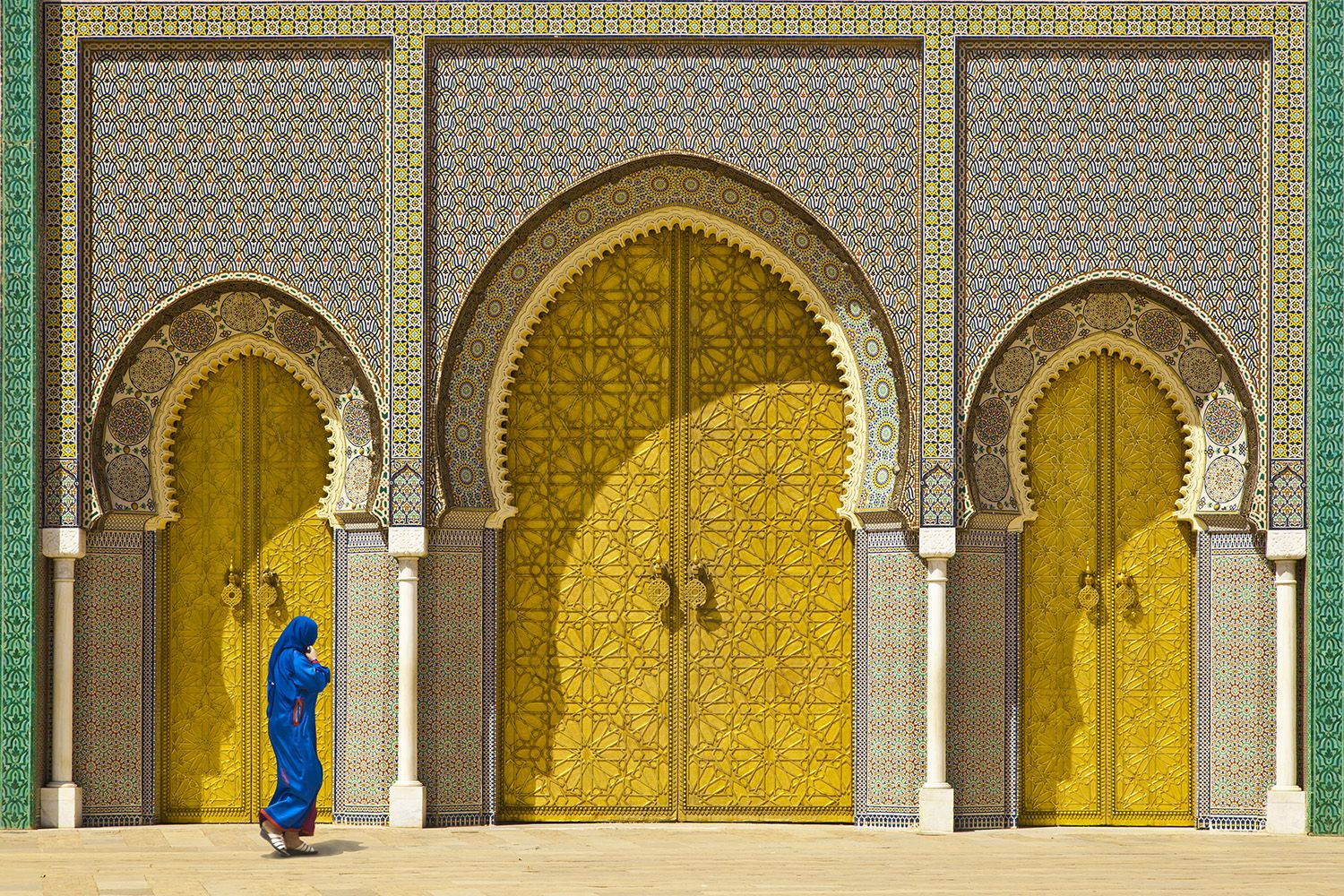 Woman walking past the golden doors of the ornate Royal Palace in Fes