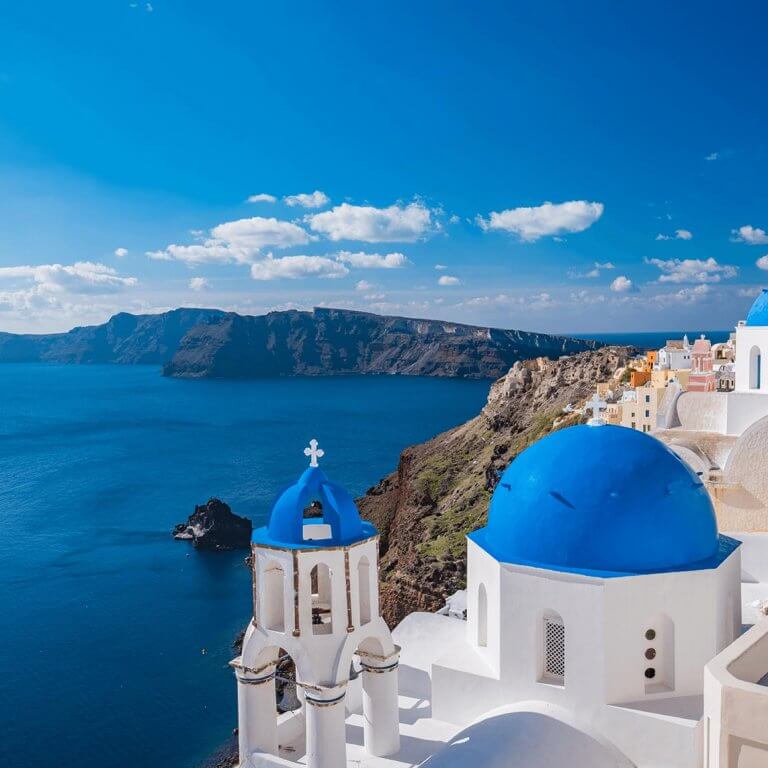 View of Santorini's blue domed white buildings, the Aegean sea, and rocky cliffs