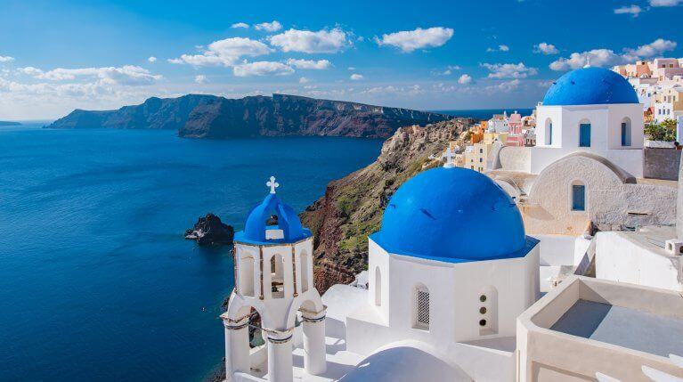 View of Santorini's blue domed white buildings, the Aegean sea, and rocky cliffs