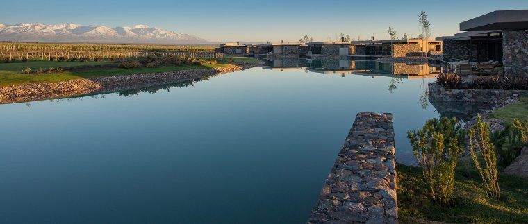 Private stone villas on a small lake by a vineyard with mountains in the distance at The Vines Resort in Mendoza, Argentina