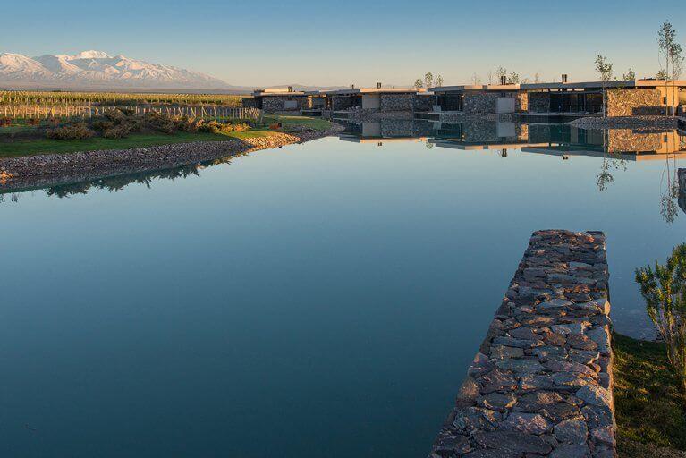Private stone villas on a small lake by a vineyard with mountains in the distance at The Vines Resort in Mendoza, Argentina