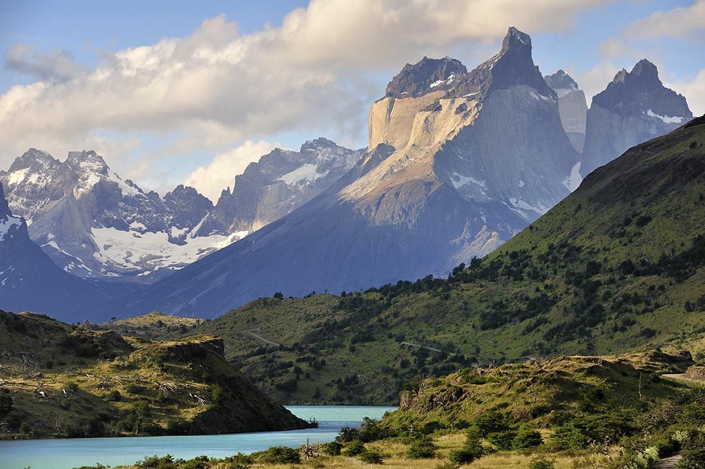 Glacial lake, green hills, and jagged peaks of the Cuernos del Paine in the distance