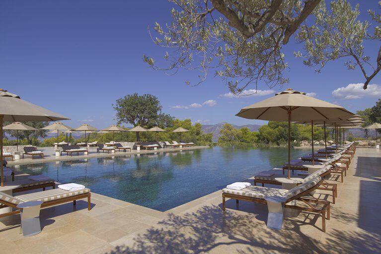 Outdoor infinity pool surrounded by sun loungers and umbrellas at Amanzoe luxury resort on Peloponnese peninsula
