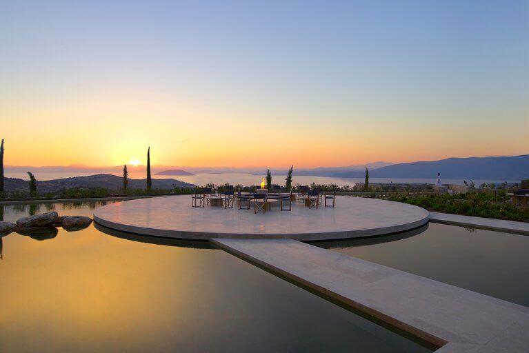 Outdoor pool with seating area in middle and view of sea at Amanzoe luxury resort on Peloponnese peninsula