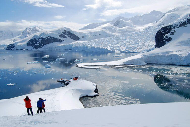 Shore excursion during a luxury yacht charter in Antarctica, trekking on the snowy terrain of Antarctica with glaciers in the distance