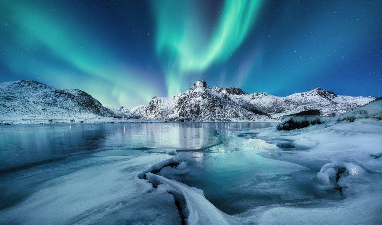 Landscape showing the icy sea and snowy mountains with the aurora borealis lighting up the sky