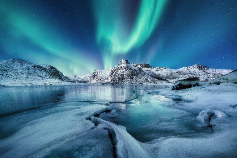 Landscape showing the icy sea and snowy mountains with the aurora borealis lighting up the sky