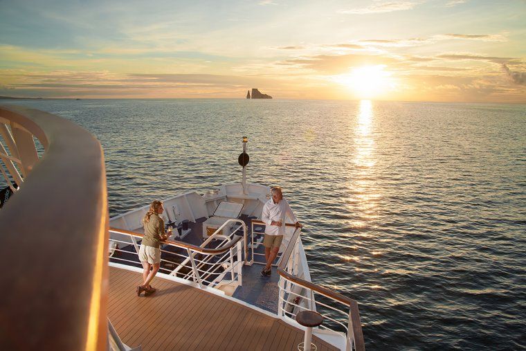 Two people stand on the bow of a yacht at sunset during Galapagos Islands luxury cruise