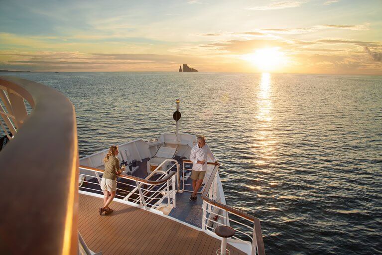 Two people stand on the bow of a yacht at sunset during Galapagos Islands luxury cruise