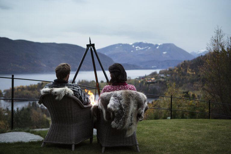Couple relaxing near a firepit admiring a view over the fjord and surrounding mountains