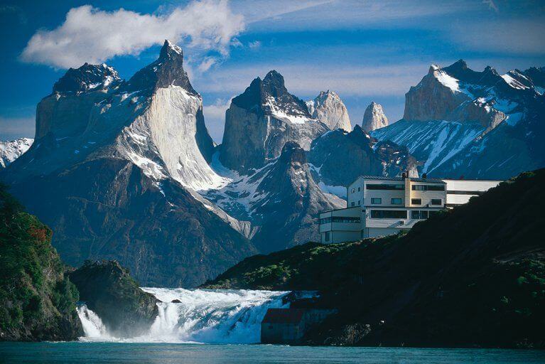 Luxury hotel Explora sits near Salto Chico waterfall with tall, jagged mountains in the distance
