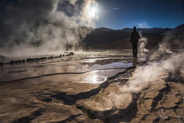 Man standing next to Geyser El Tatio with mist on a luxury Chile tour