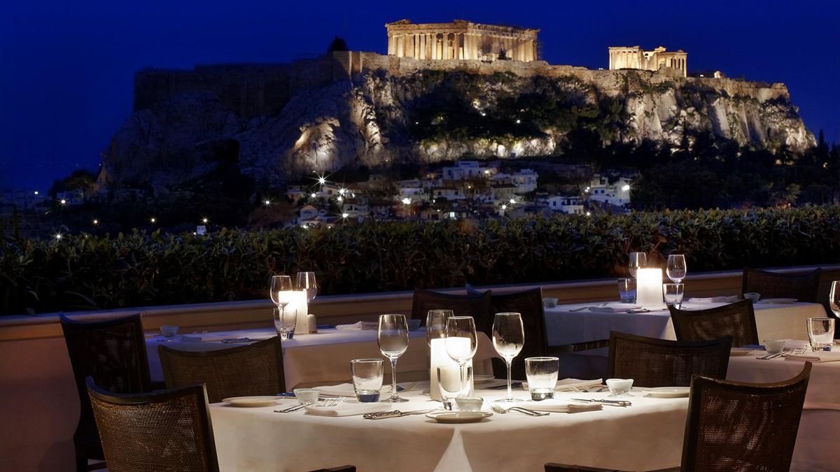 Tables set for a gourmet dinner after dark with view of lit up Acropolis