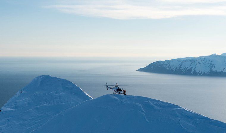 Helicopter hovering above snowy mountains and inlets of Iceland