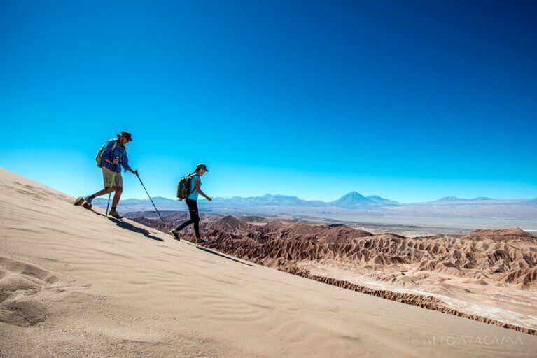Two people hike down sand dunes in the Atacama Desert