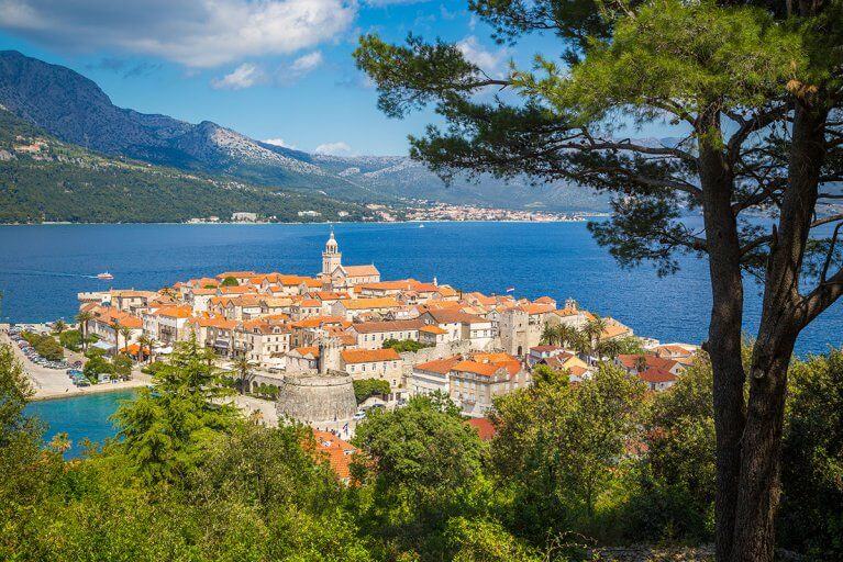 Korčula Old Town seen from forested hillside with Adriatic sea and mountains in background
