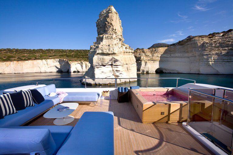 Sundeck with jacuzzi on privately chartered luxury yacht sailing near rocky cliffs in the Aegean sea