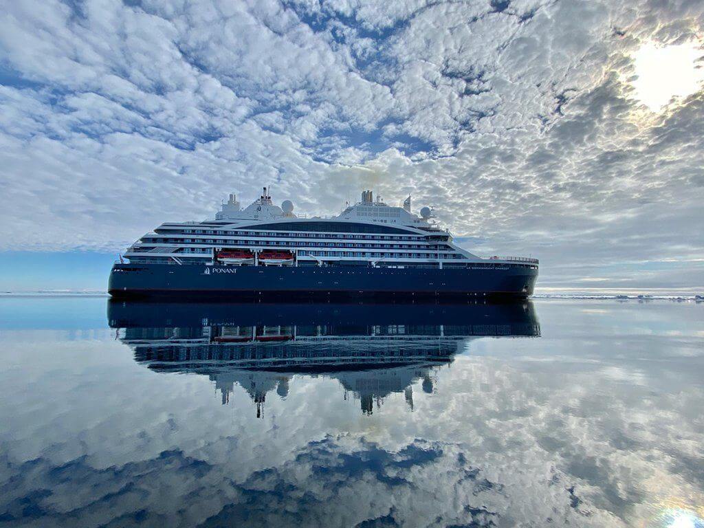 The Commandant Charcot cruisint in Antarctica, with the sky reflected in the water below