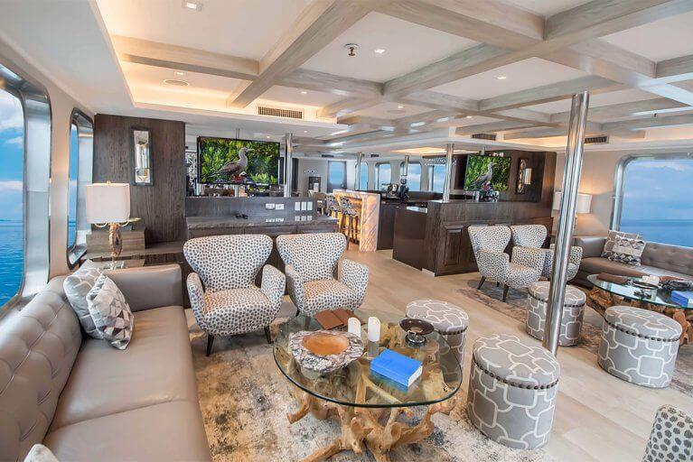 Large interior saloon with various sofas, chairs, and a bar on a private luxury yacht sailing in the Galapagos Islands