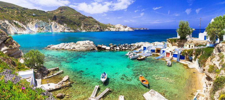 Clear waters and rocky beach by blue and white village of Mandrakia on Milos island in Cyclades archipelago