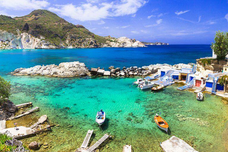 Clear waters and rocky beach by blue and white village of Mandrakia on Milos island in Cyclades archipelago