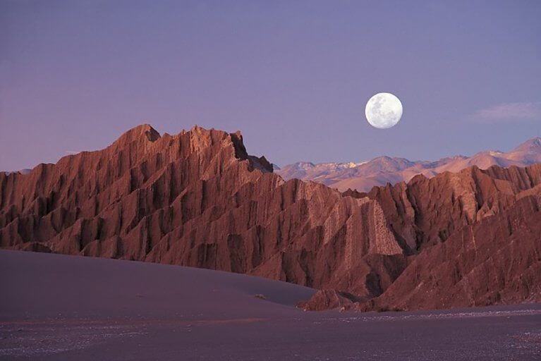 Red mountains in Moon Valley in the Atacama Desert with full moon in night sky