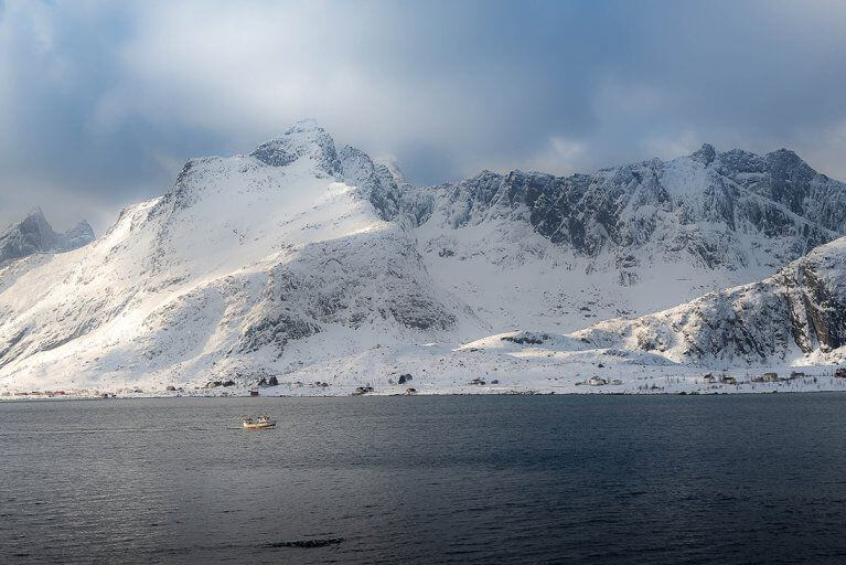 Panoramic landscape of a snowy fjord with a fishing boat small against snowy mountains