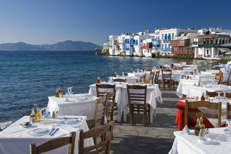 Tables set by the seaside with views of white buildings on Mykonos