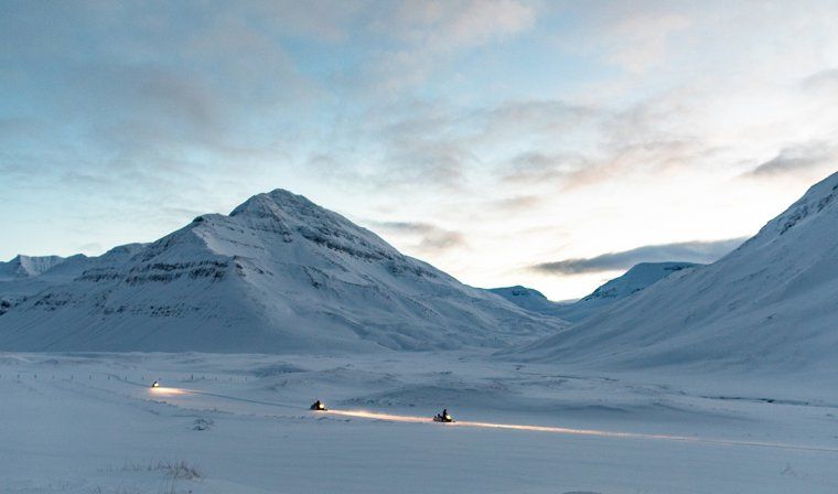 Snowmobiling excursion at dusk in Iceland, with headlights lighting up the landscape