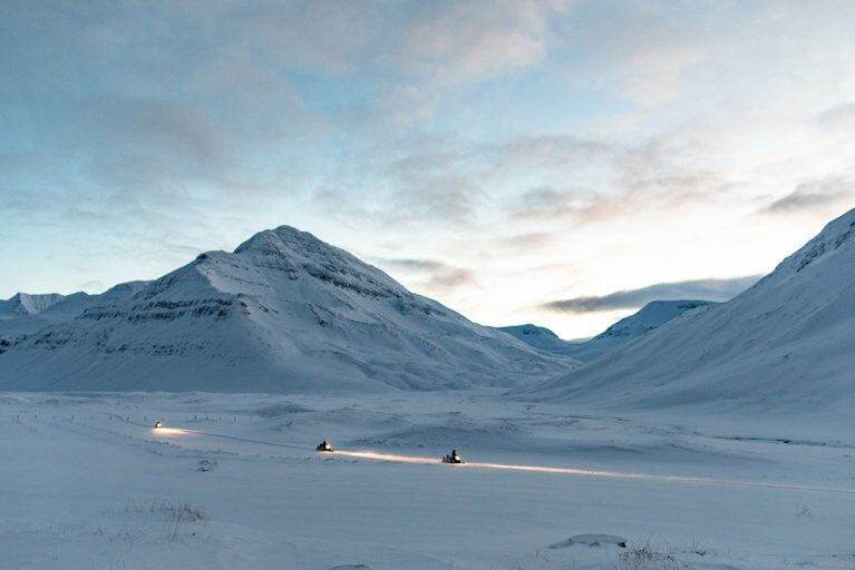 Snowmobiling excursion at dusk in Iceland, with headlights lighting up the landscape