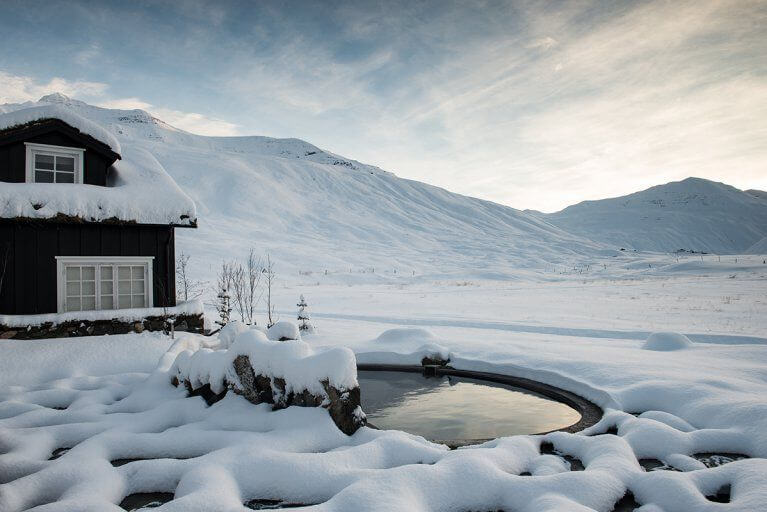 Small geothermal pool near building in snowy Icelandic countryside