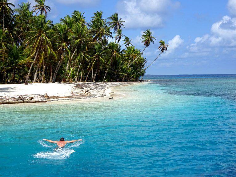 Man swims in clear blue waters near island in San Blas, Panama