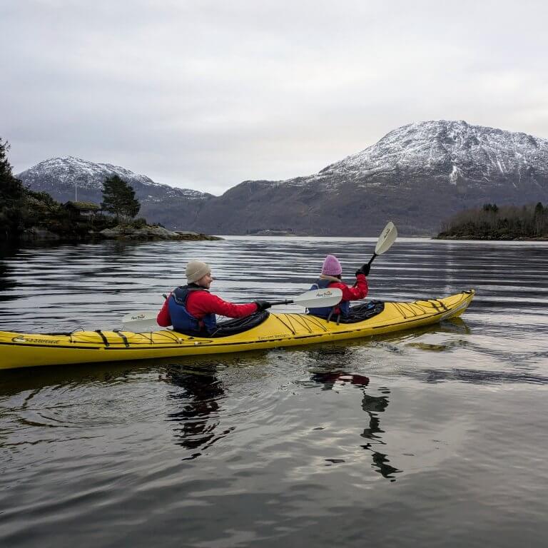 Two travelers kayaking across a fjord during an Arctic adventure tour in Norway