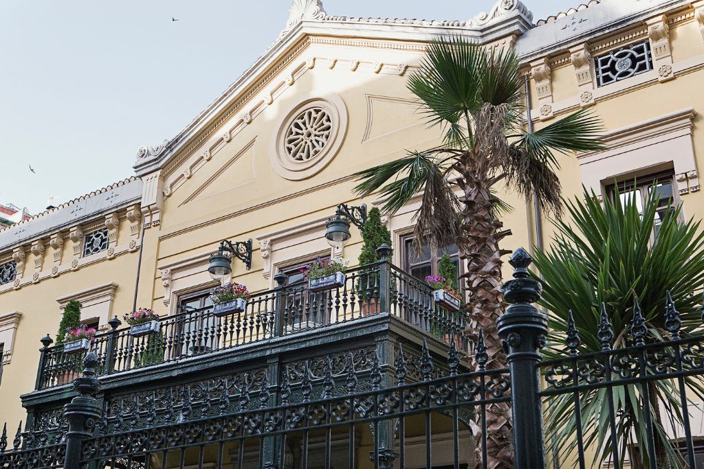 The white exterior of Hospes Palacio de los Patos with a palm tree outside it.