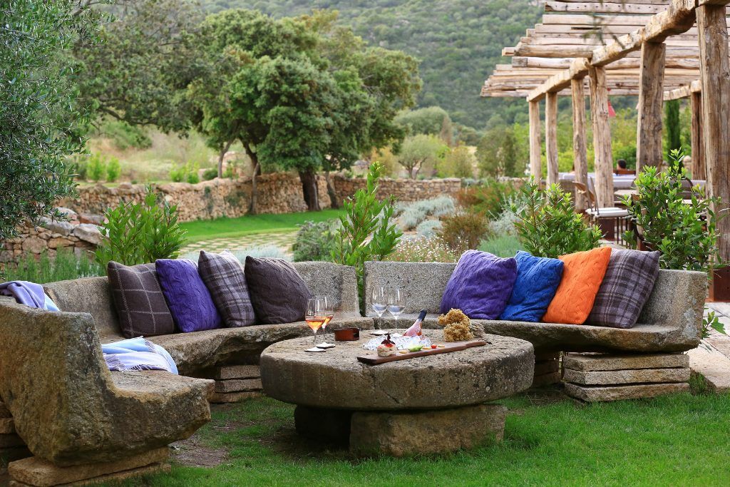 An outdoor wooden table with a wooden sofa with colorful cushions on it at Domaine de Murtoli.