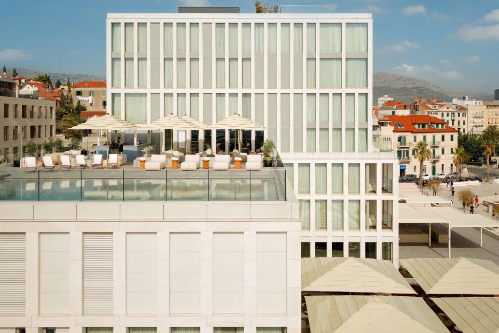 The exterior of the Ambassador Hotel and a rooftop with loungers.