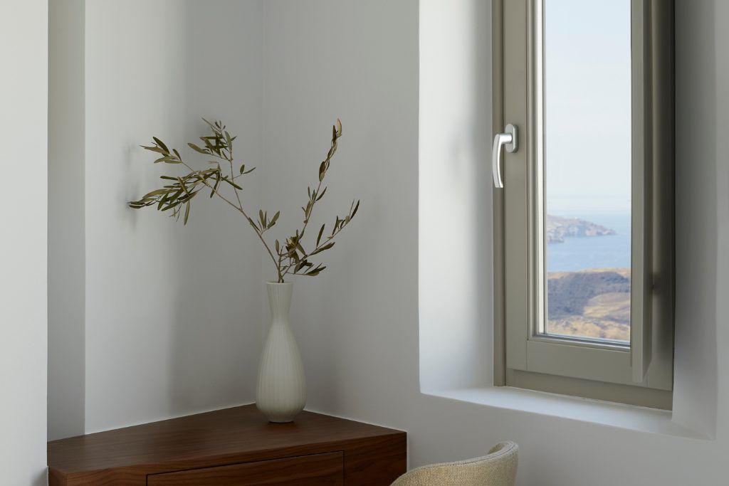 A vase on a table next to a window in one of the rooms at The Grace Santorini