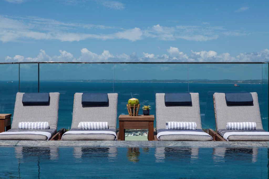Lounge chairs next to a rooftop swimming pool overlooking the ocean.