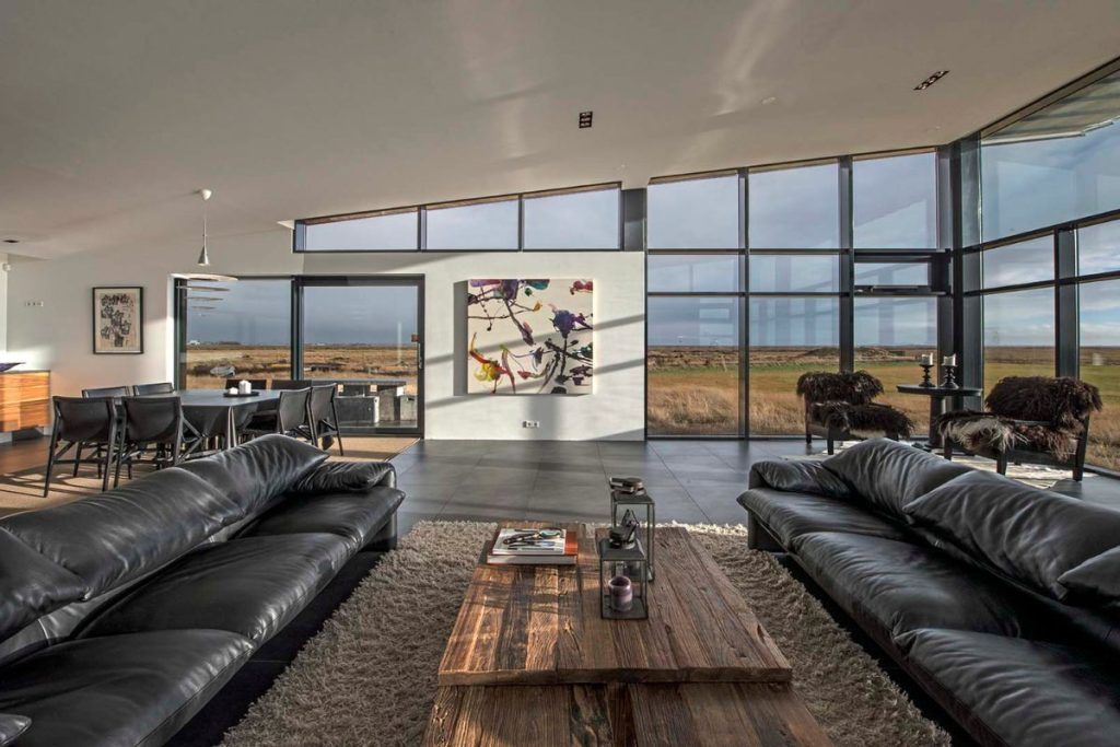 A panoramic living room with two leather couches and a wooden coffee table in a private villa in Southern Iceland.