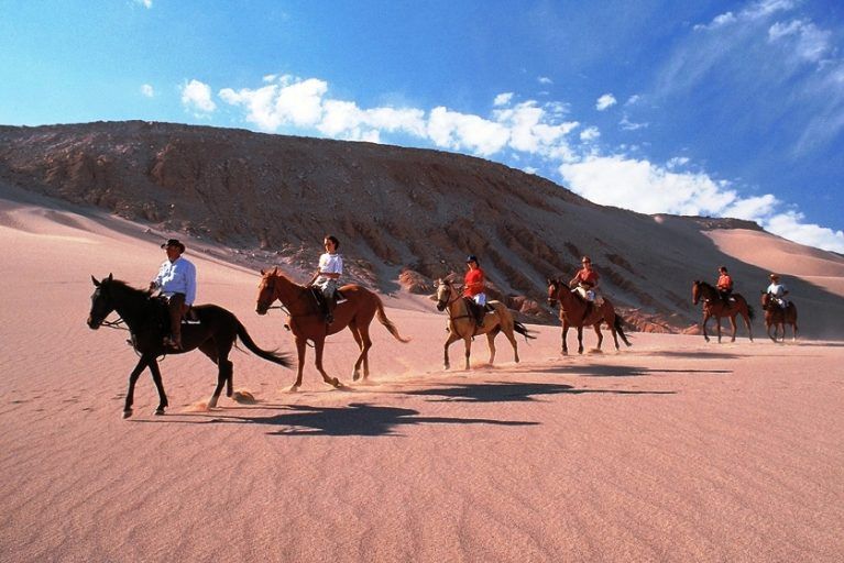 A group of people riding horses through the Atacama Desert.