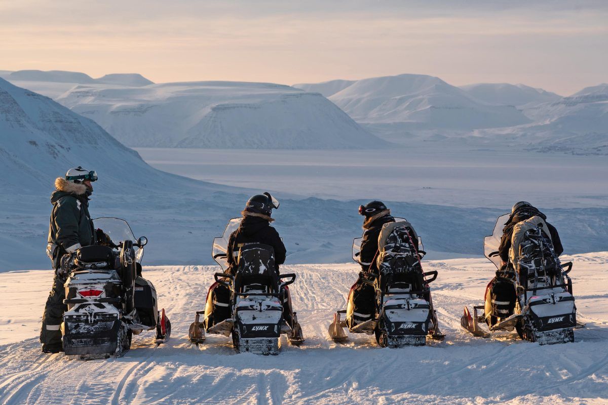 Four people in a row on snowmobiles in Svalbard.