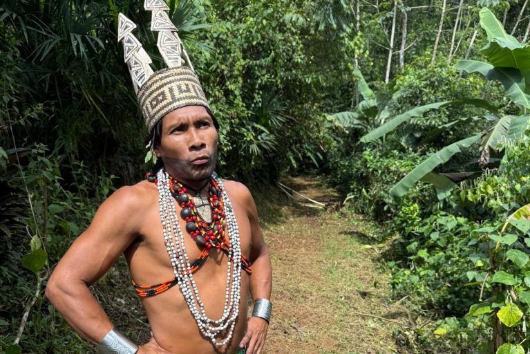 An Emberá man with a tall hat standing in a forest.