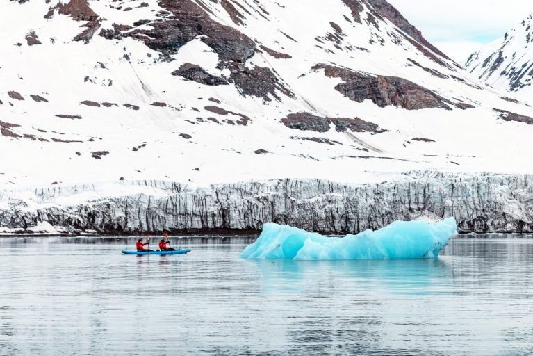 People kayaking past an iceberg in Svalbard